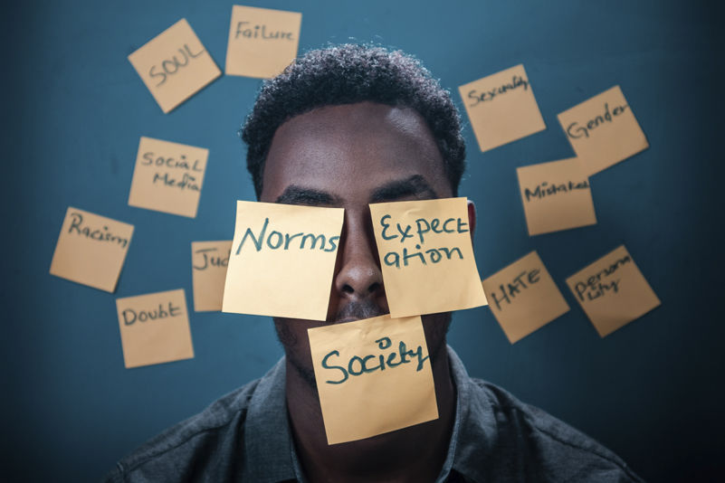 A man with sticky notes on his face, with the words "Norms", "Expectations" and "Society".