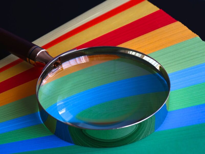 A magnifying glass resting on a colourful striped surface, enlarging a section to reveal intricate details. The image symbolises focus, clarity, and the importance of examining things closely.