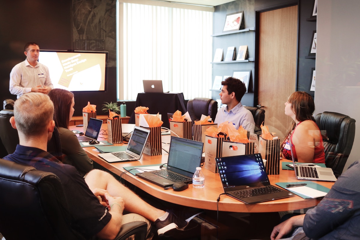 Team gathered in a conference room with laptops, participating in a collaborative daily huddle or stand-up meeting, focused on alignment, task priorities, and problem-solving to improve productivity and teamwork