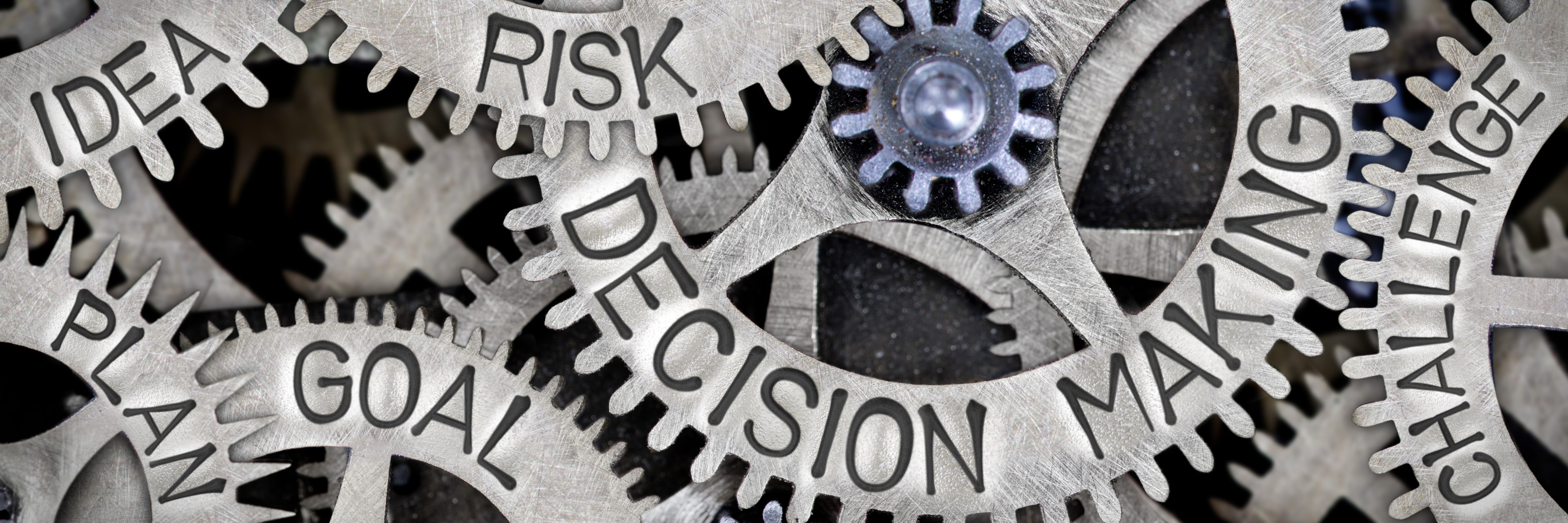 Close-up of interlocking metal cogs engraved with words like 'Decision Making,' 'Risk,' 'Goal,' 'Plan,' and 'Challenge,' representing the interconnected elements of the decision-making process